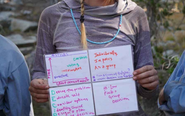 a person holds a small whiteboard as part of a lesson on group dynamics on an outward bound course